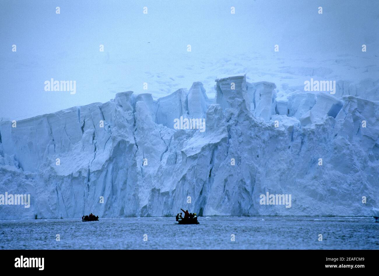 Big glacier with high ice wall being visited by tourists in a zodiac on Antarctica Stock Photo
