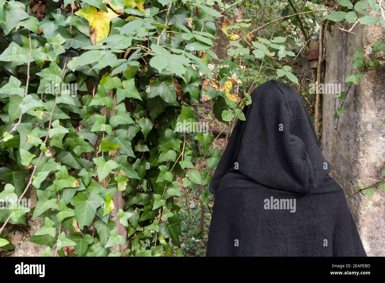 Rear view of woman with black cloak with hood in ruined building Stock Photo