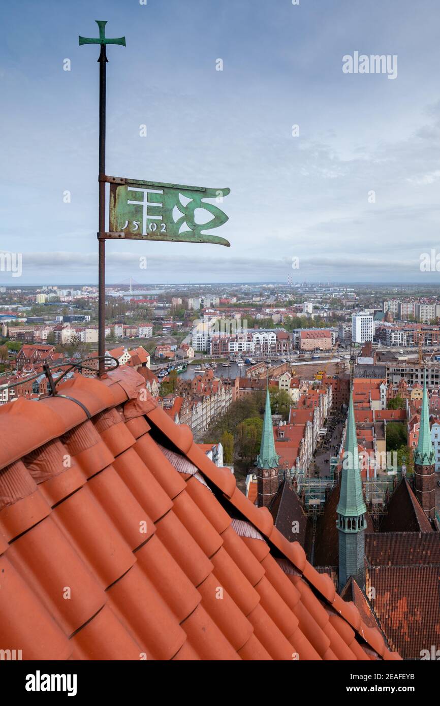 Cityscape viewed from the top of a cathedral tower with red roof and green metal banner in the foreground. Spring in the city of Gdansk, Poland. Stock Photo