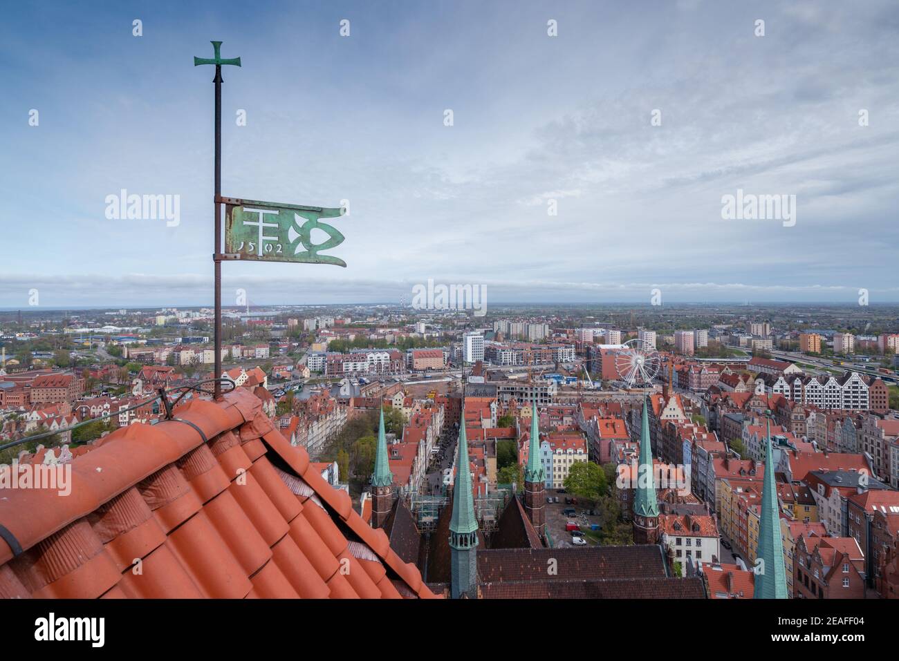 Cityscape viewed from the top of a cathedral tower with red roof and green metal banner in the foreground. Spring in the city of Gdansk, Poland. Stock Photo