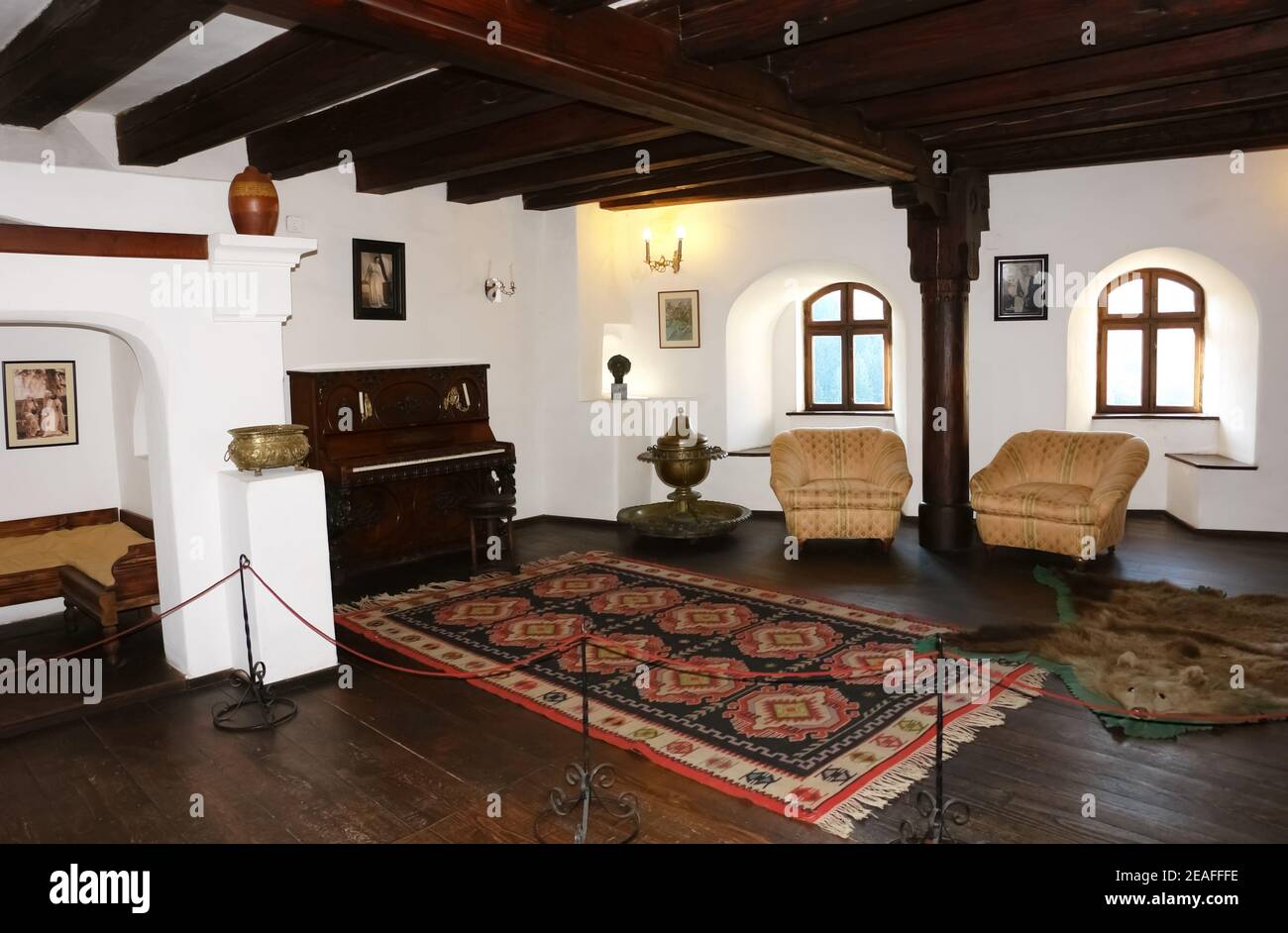 The interior of a large room in an old castle with two windows, carved wooden furniture, a piano and two armchairs. Stock Photo