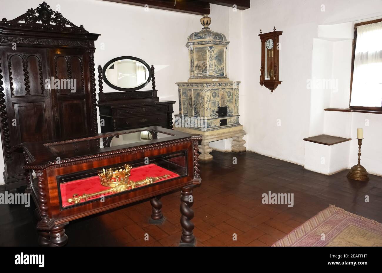 Interior of a room with an old tiled stove, carved wooden furniture, a golden crown and a scepter. Stock Photo