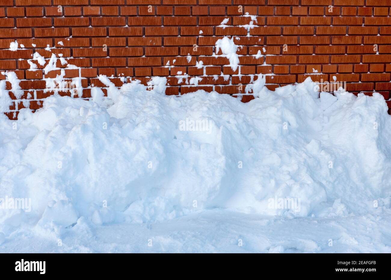 Snow snowdrift against a brick wall. Snow removal. Stock Photo