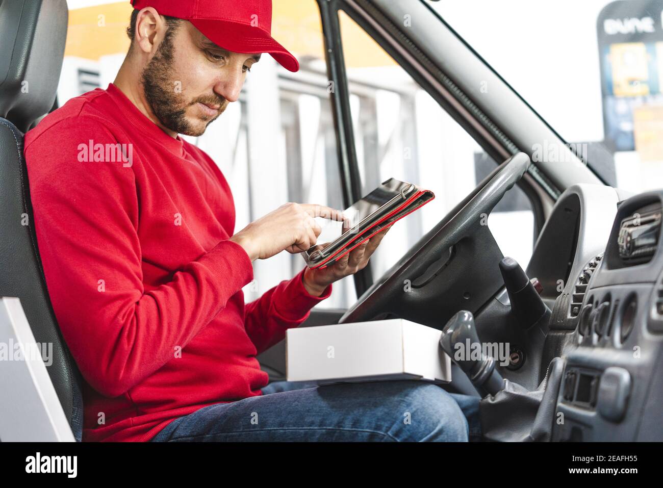 Delivery man registering the details of the product with a tablet while sitting on the driver's seat Stock Photo