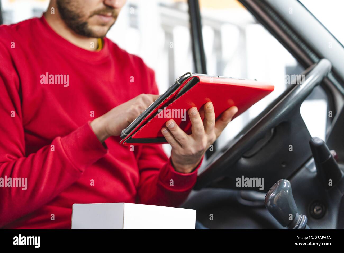 Delivery man registering the details of the product with a tablet while sitting on the driver's seat Stock Photo