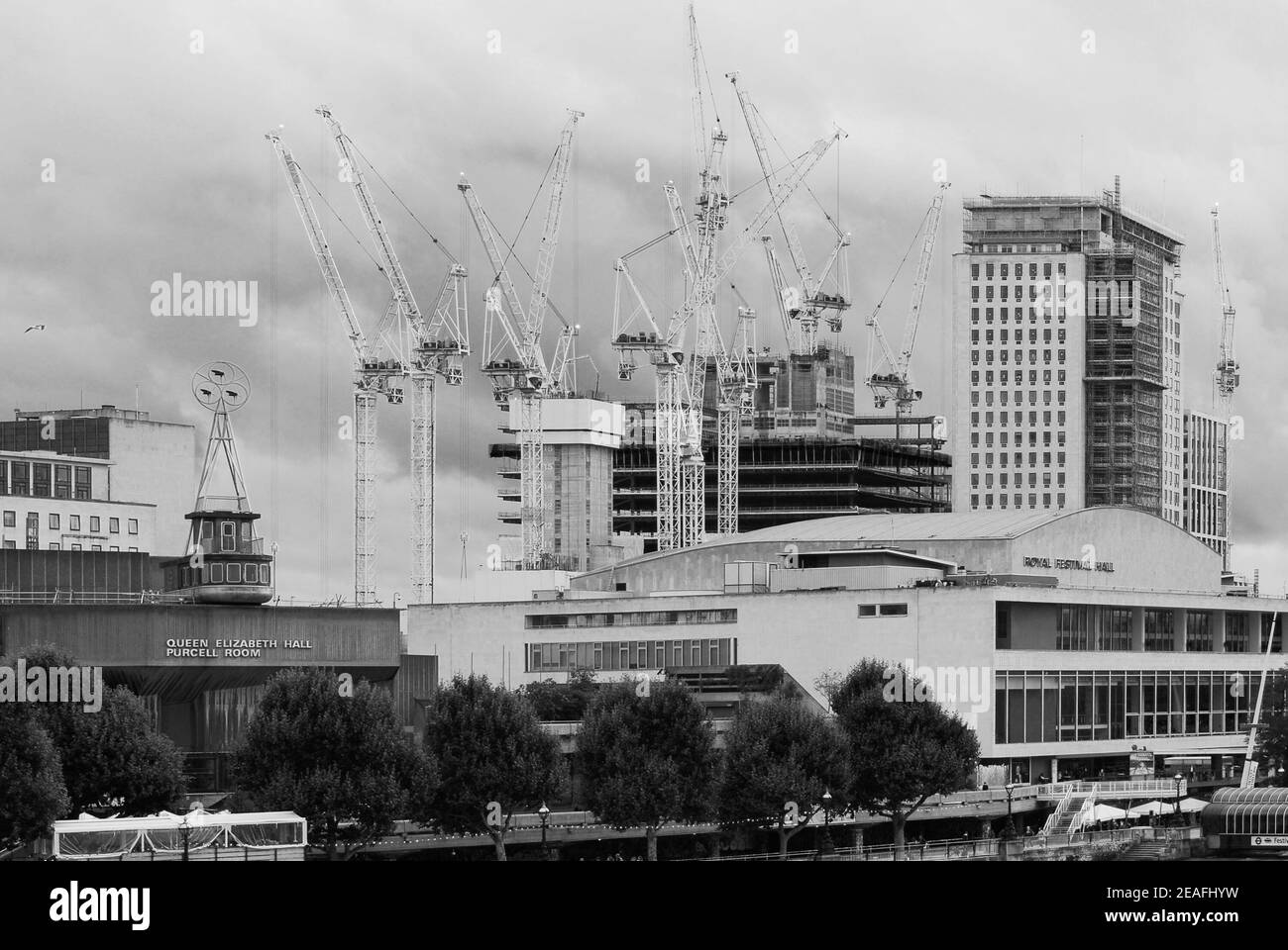 Monochrome image of cranes dominating the South Bank skyline, behind the Royal Festival Hall on the banks of the River Thames in London. Stock Photo