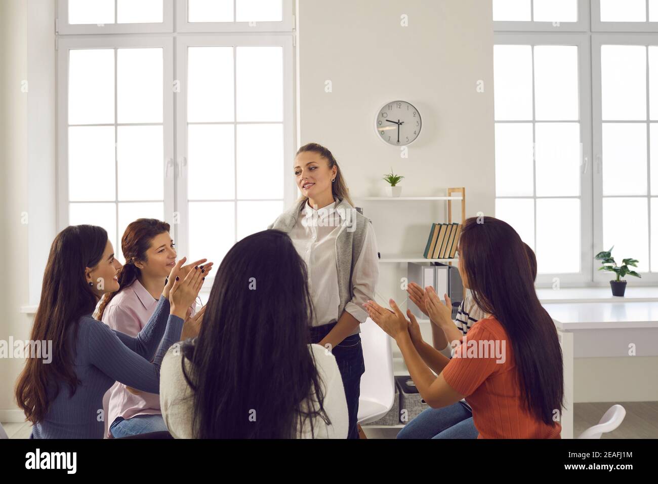 Team of supportive women applauding colleague for presentation in corporate meeting Stock Photo
