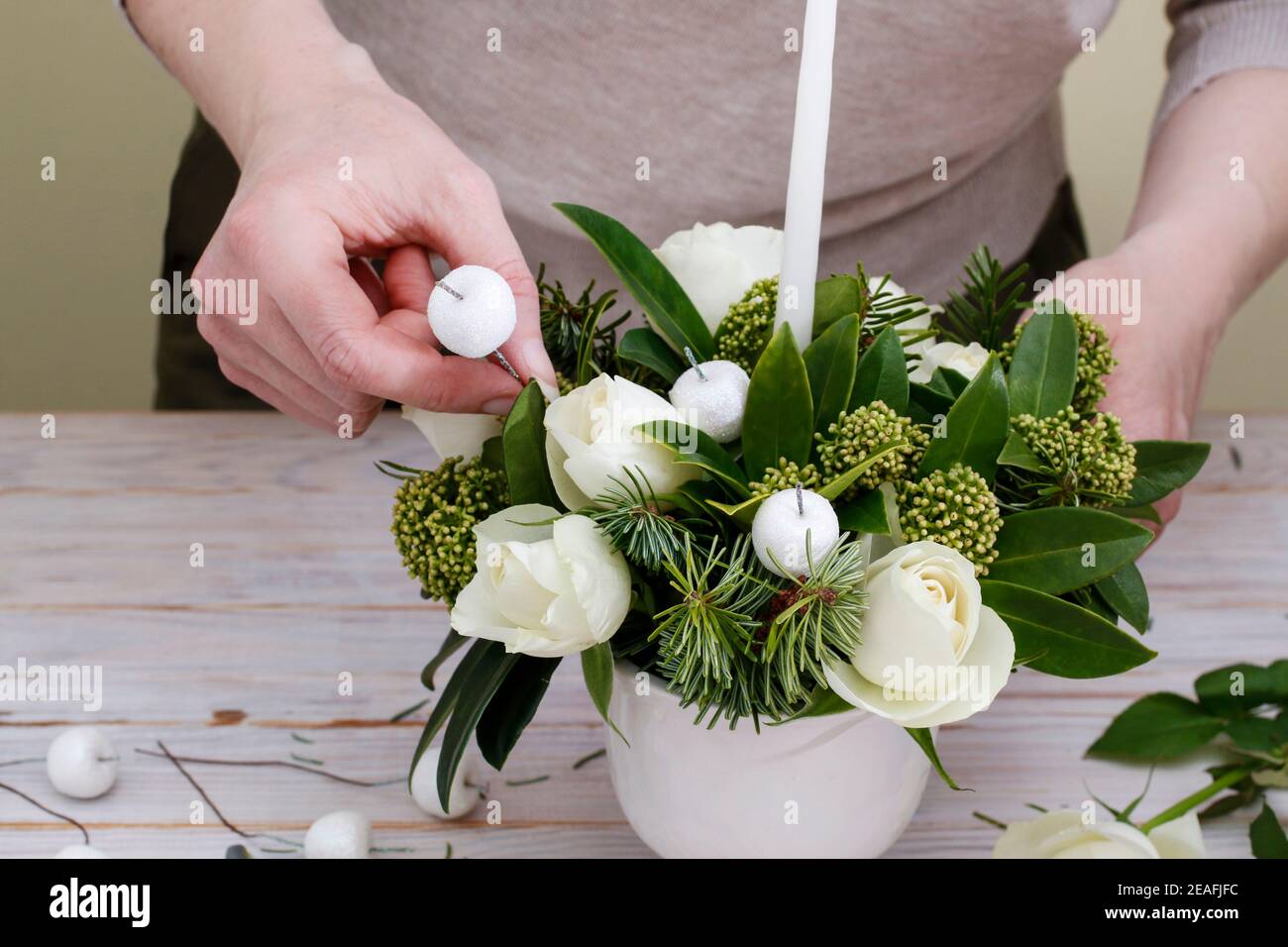 Florist at work: woman shows how to make floral arrangement with white roses, skimmia, an evergreen shrub, and fir twigs. Step by step, tutorial. Stock Photo