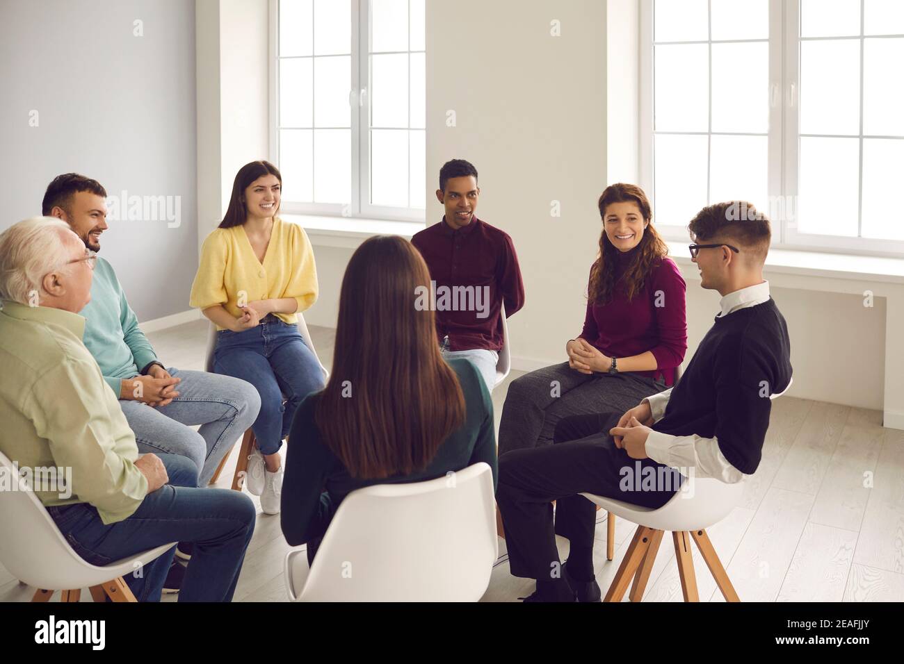 Smiling diverse people listening to young man sharing his story in a group therapy session Stock Photo
