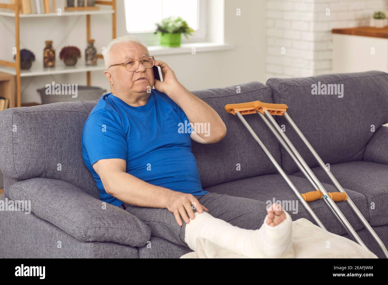 Senior man with broken leg sitting on couch and talking to doctor or