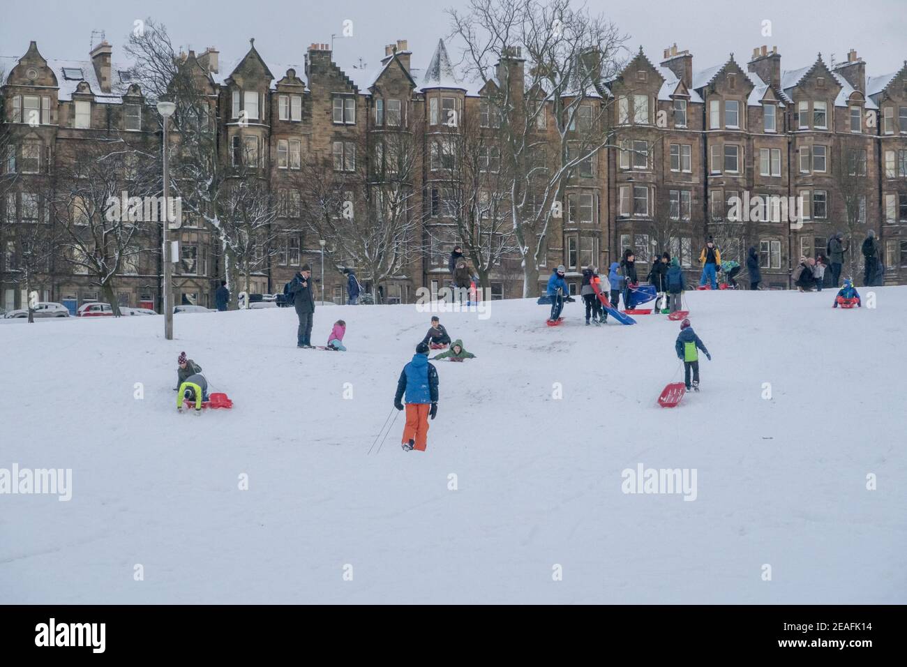 Children playing in the snow with sledges at the Edinburgh meadows in front of tenement building Stock Photo