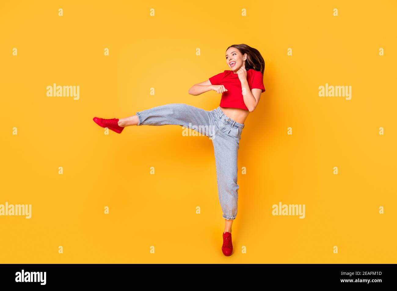Boxer girl practicing air kicks raise leg jumping high wear red crop top jeans isolated yellow color background Stock Photo