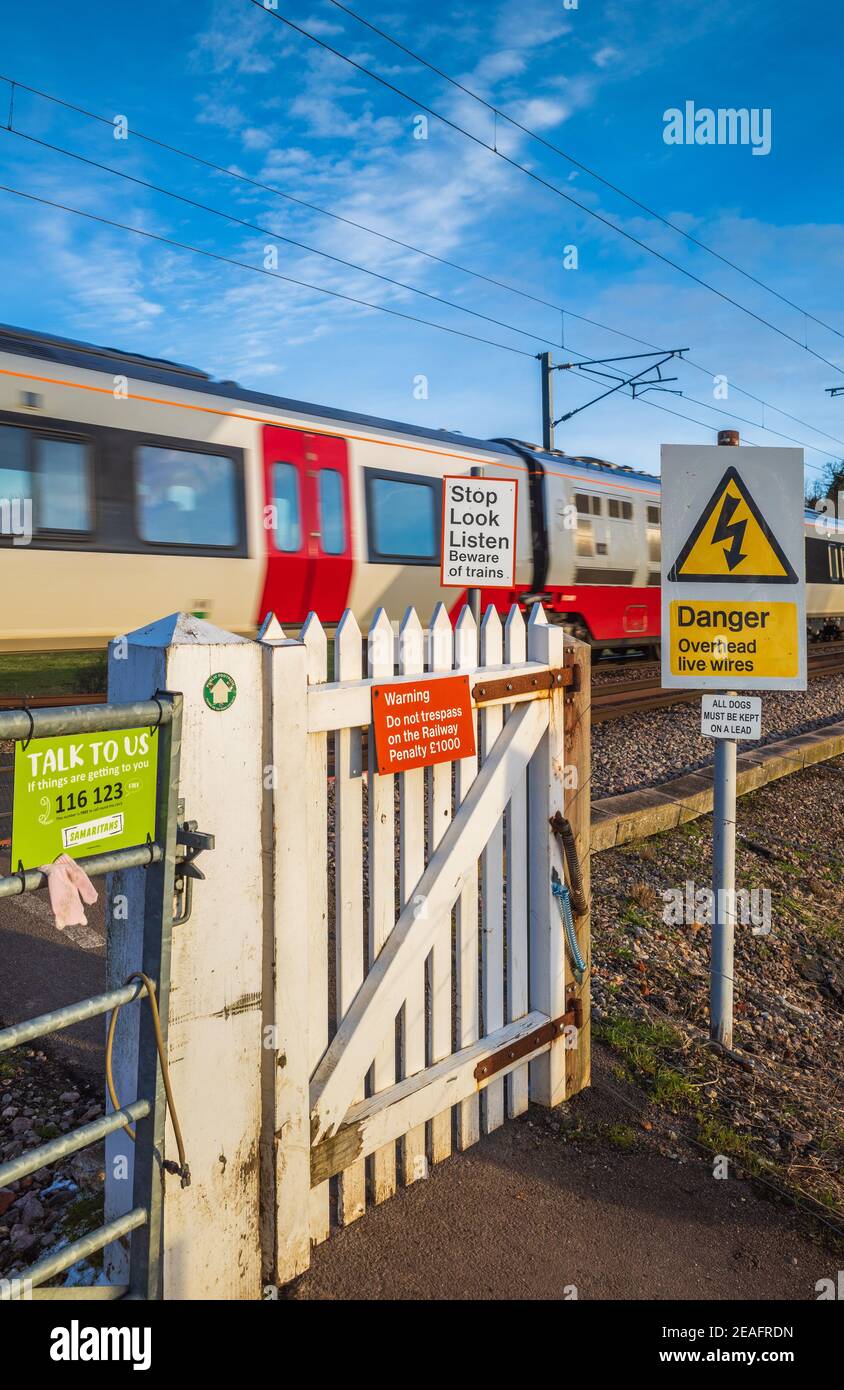 Pedestrian Train Crossing Gate with passing Greater Anglia train - unautomated Level crossing for pedestrians with warning signs. Stock Photo