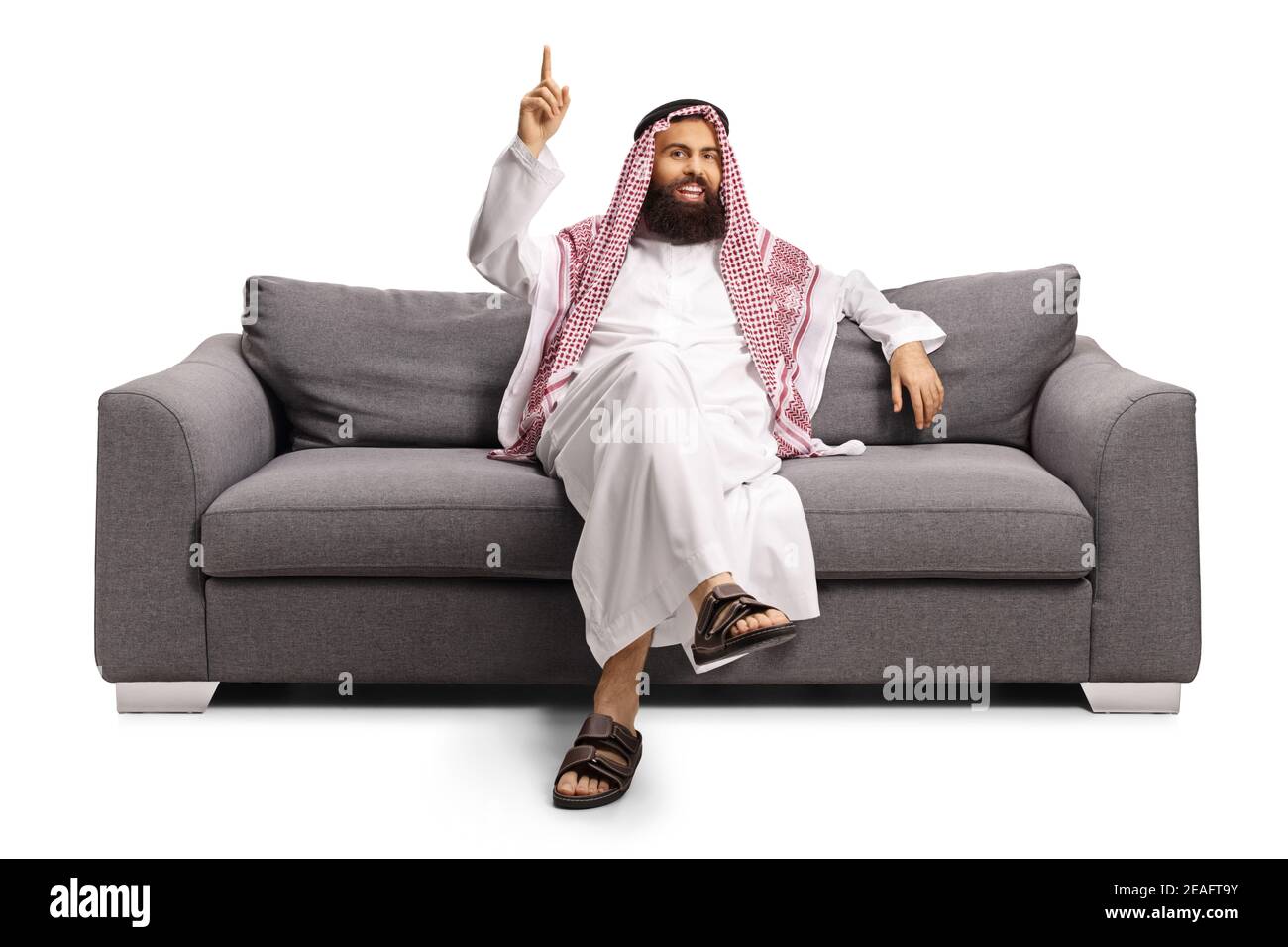 Saudi arab man in a thobe sitting on a sofa and pointing up isolated on white background Stock Photo