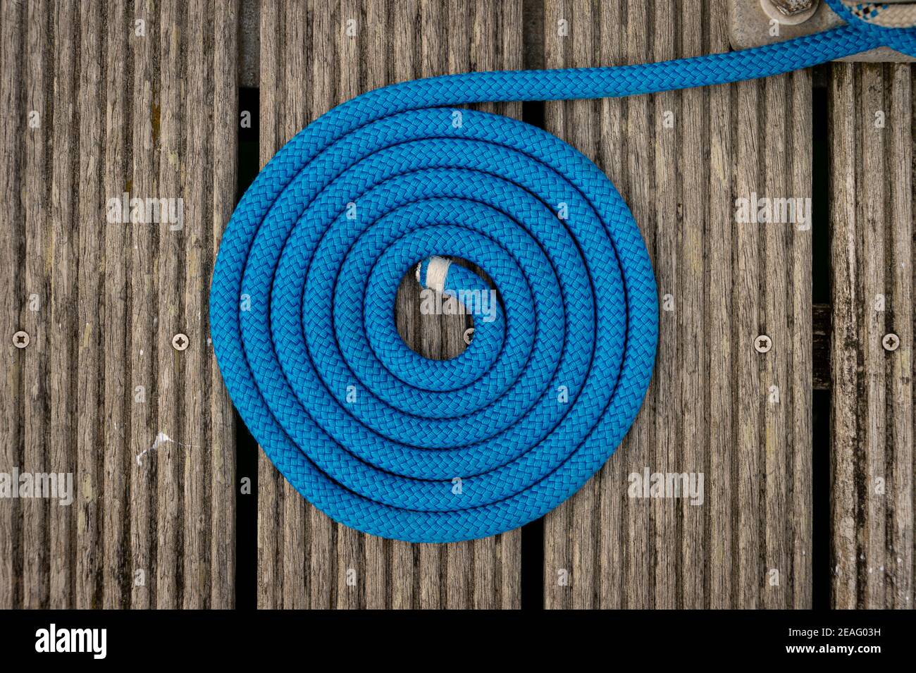 coil of blue mooring rope on a wooden jetty. Photographed directly above. Stock Photo