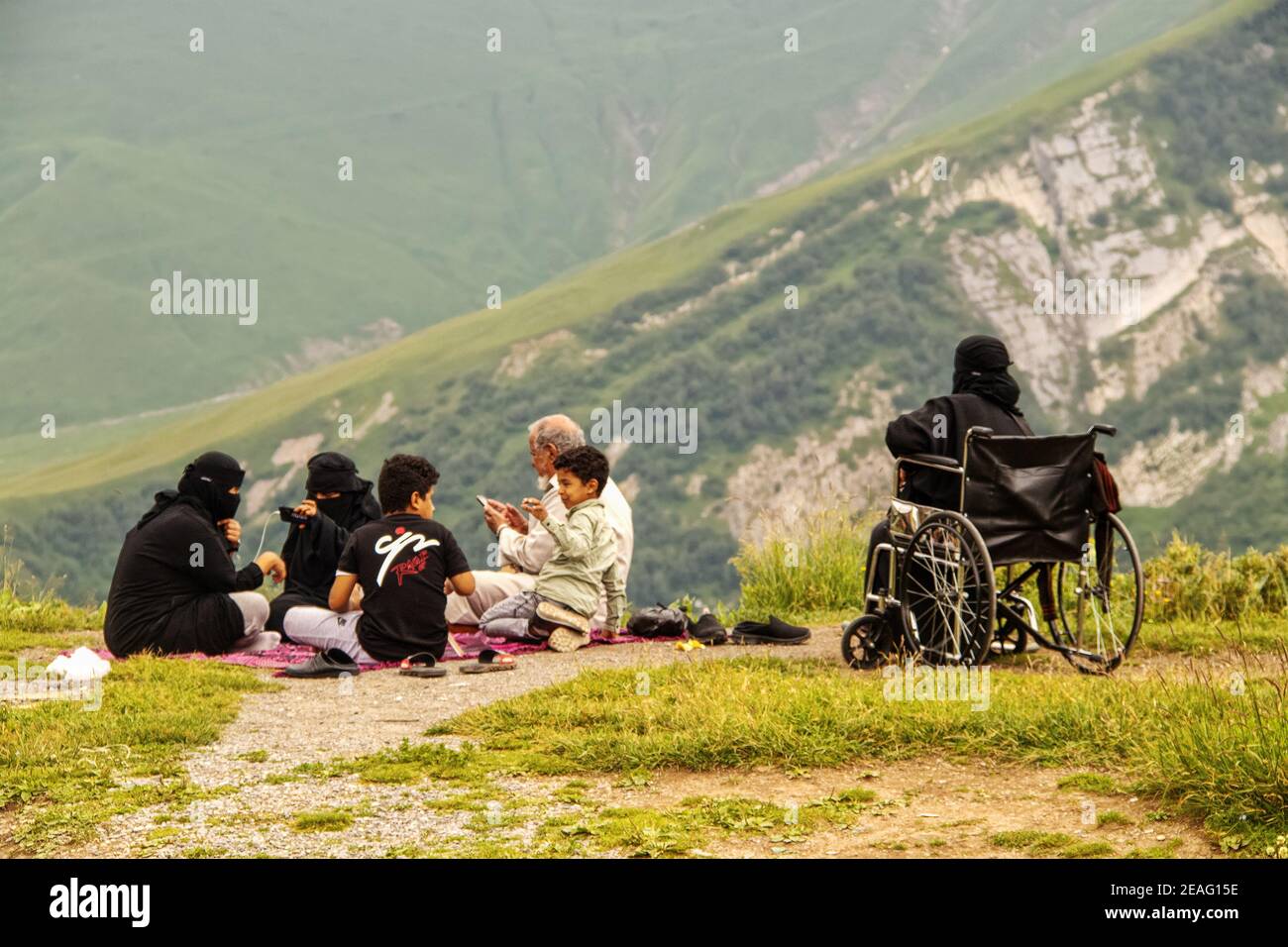 6-16-2019-Military Highway, Georgia - Family in islamic dress with mobile phones - woman in wheelchair sits on cliff of Devil's Valley in Caucasus mou Stock Photo