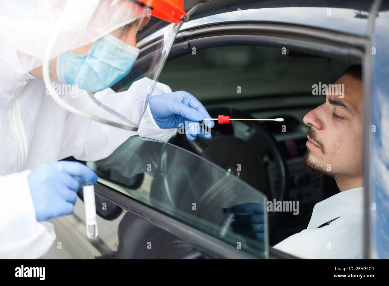 Drive-thru Coronavirus COVID-19 test,paramedic in personal protective equipment & face shield performing nasal swab through car window on male patient Stock Photo