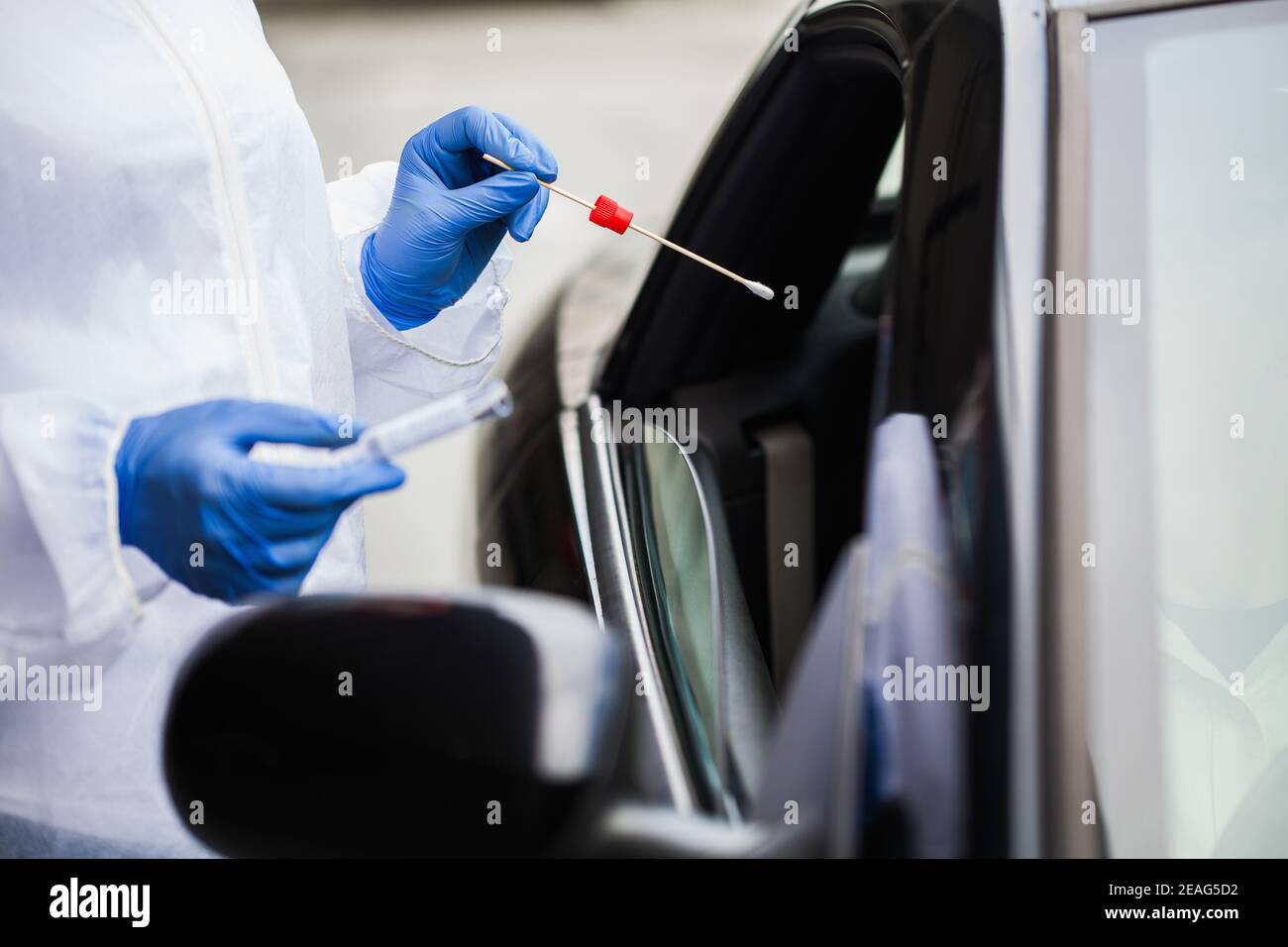 Medical worker in N95 PPE performing nasal & throat swab on person in vehicle through car window,COVID-19 UK NHS mobile testing centre drive thru Stock Photo