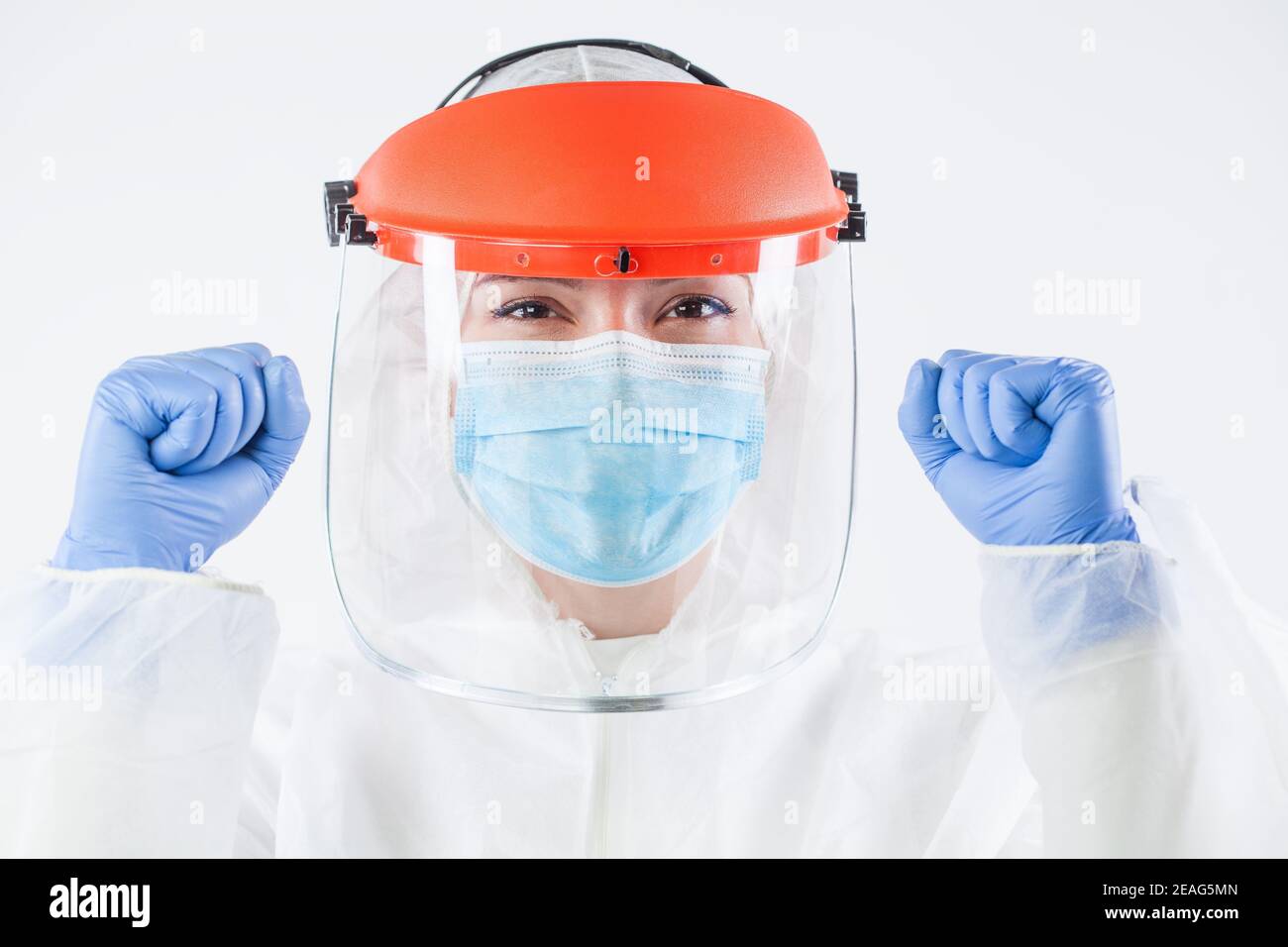 Healthcare professional in personal protective equipment, wearing surgical gloves, face shield, white protective hazmat biohazard suit, clenched fists Stock Photo