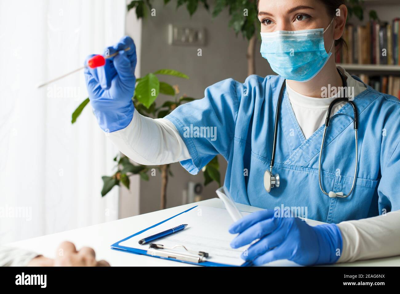 Female caucasian doctor holding a swab collection stick, nasal and oral specimen swabbing in doctor's office, patient PCR testing procedure appointmen Stock Photo