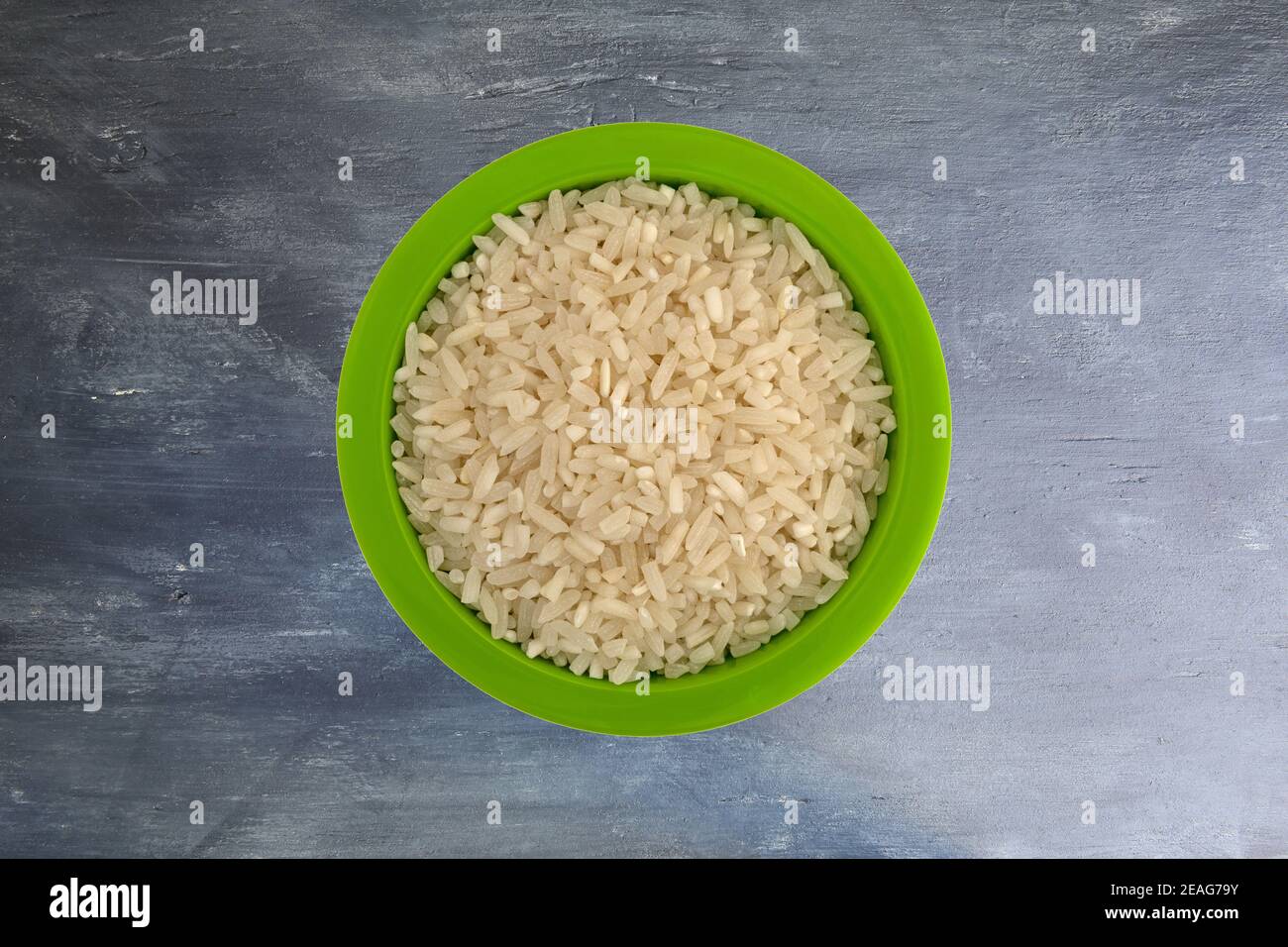 Top view of enriched long grain rice in a small green bowl on a wood painted gray background. Stock Photo