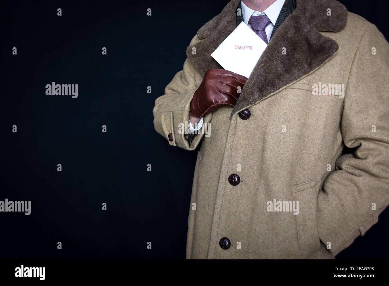 Portrait of Man in Fur Coat and Leather Gloves Pulling Confidential Envelope out of Pocket on Black Background. Film Noir Secret Agent Spy. Stock Photo