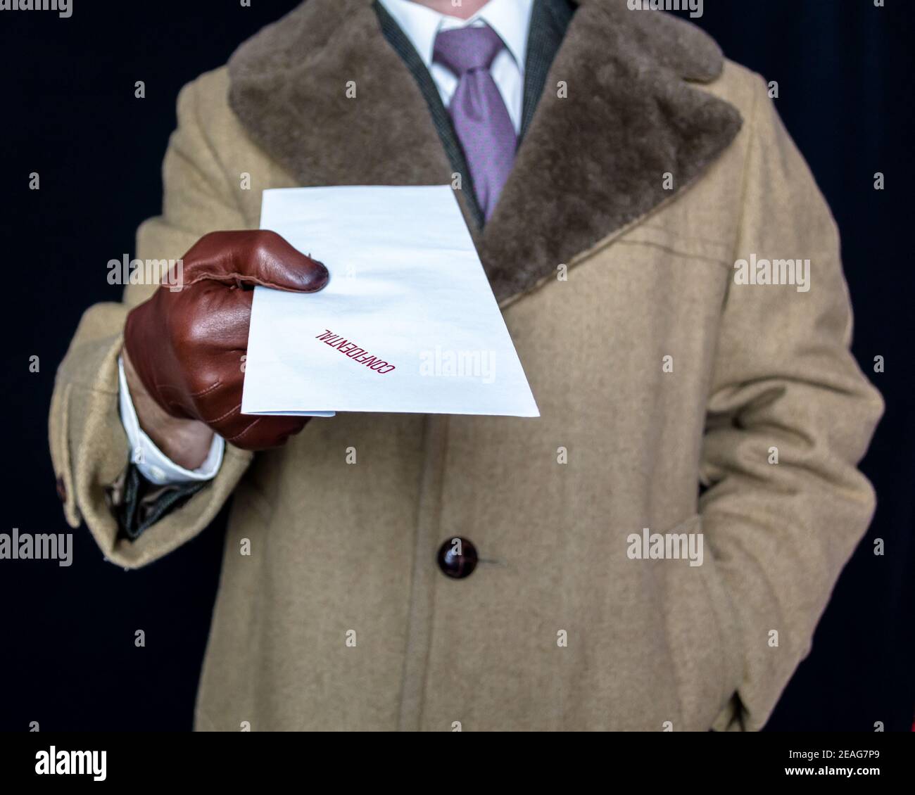 Portrait of Man in Fur Coat and Leather Gloves Handing Over  Confidential Envelope on Black Background. Film Noir Secret Agent Spy. Theft and Crime. Stock Photo