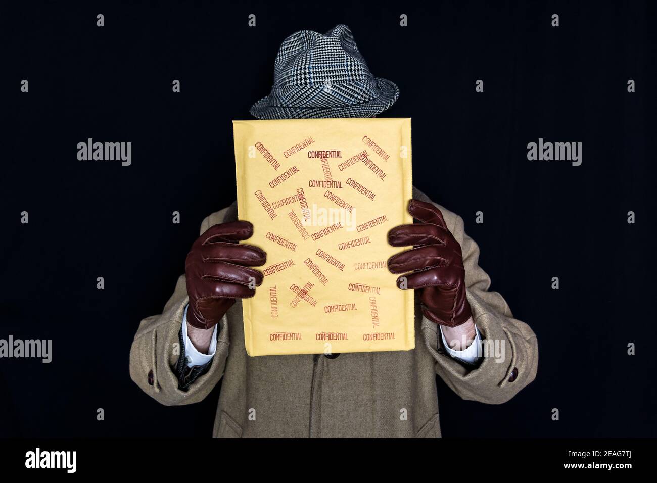 Portrait of Man in Coat and Hat Holding Confidential Envelope Over His Face on Black Background. Film Noir Secret Agent Spy. Identity Theft and Crime. Stock Photo