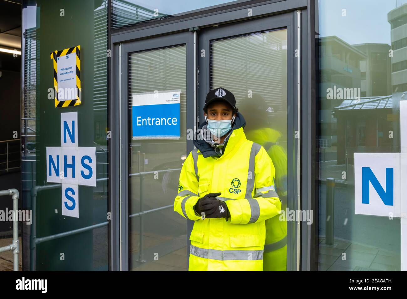 Greeter in a yellow hivis jacket outside the entrance to the NHS Covid