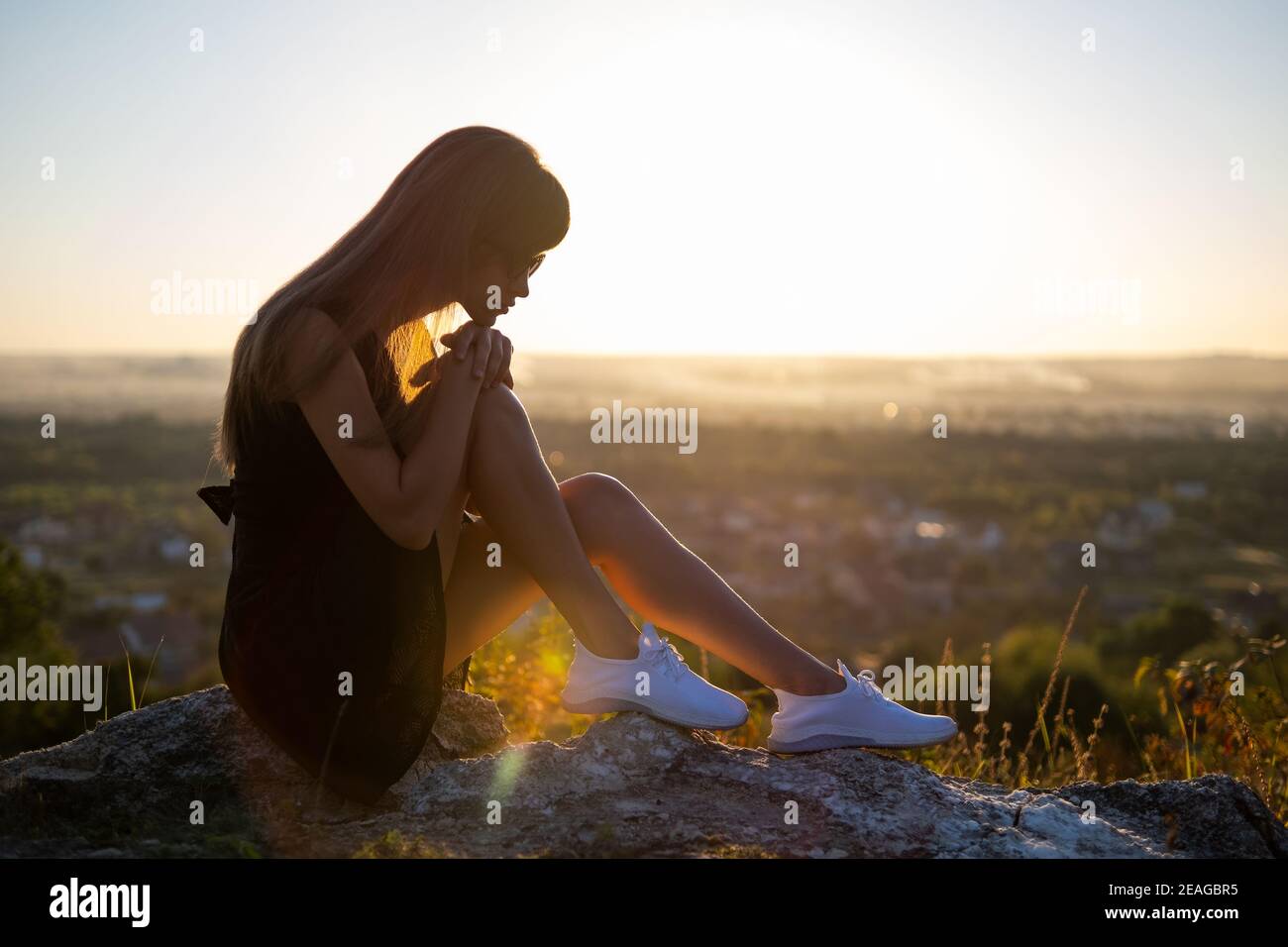 Young depressed woman in black short summer dress sitting on a mountain ...