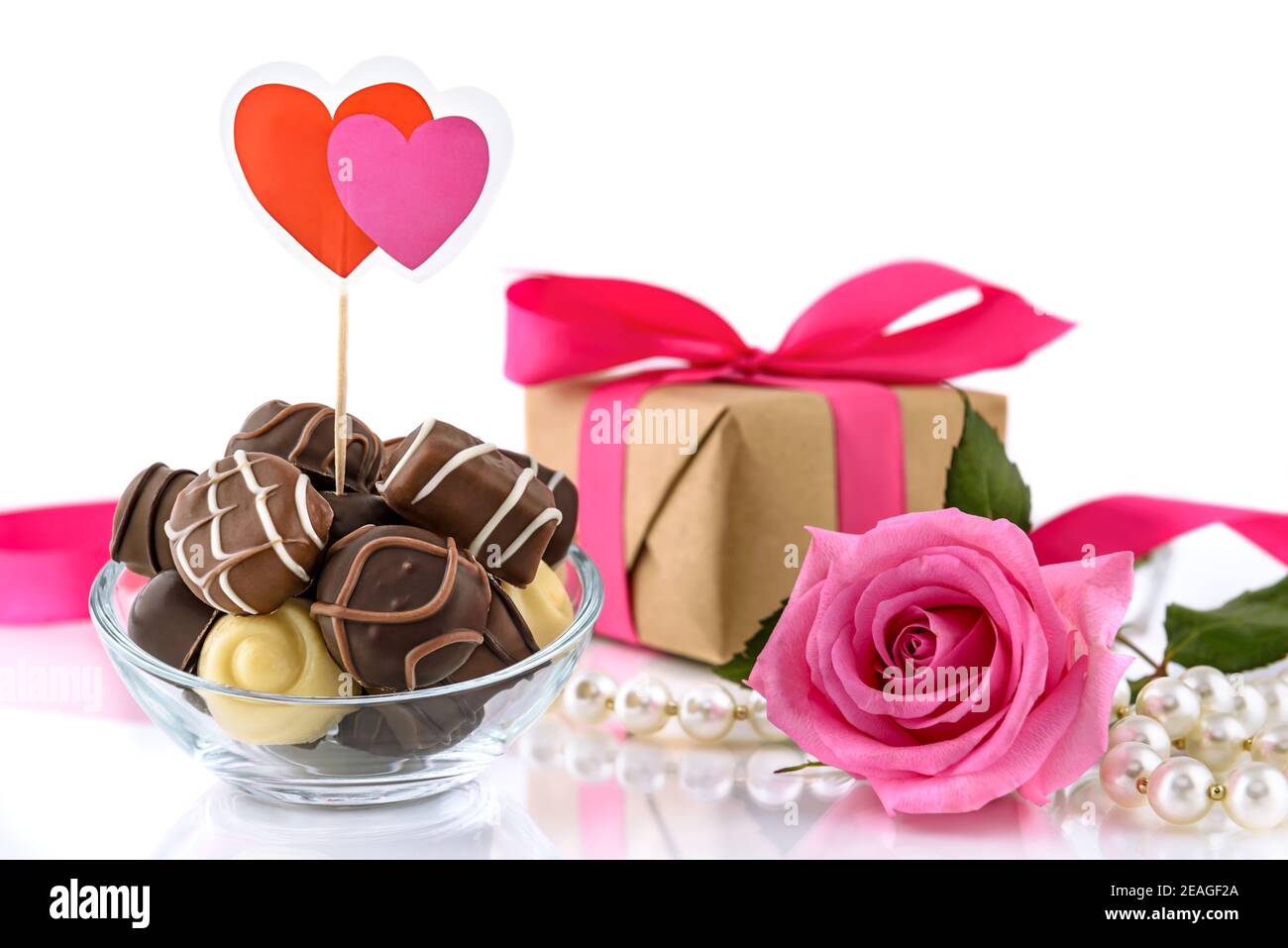 Chocolate pralines, gift box, bouquet of pink roses and string of pearls on the white background. Valentine's Day and Women's Day concept, selective f Stock Photo