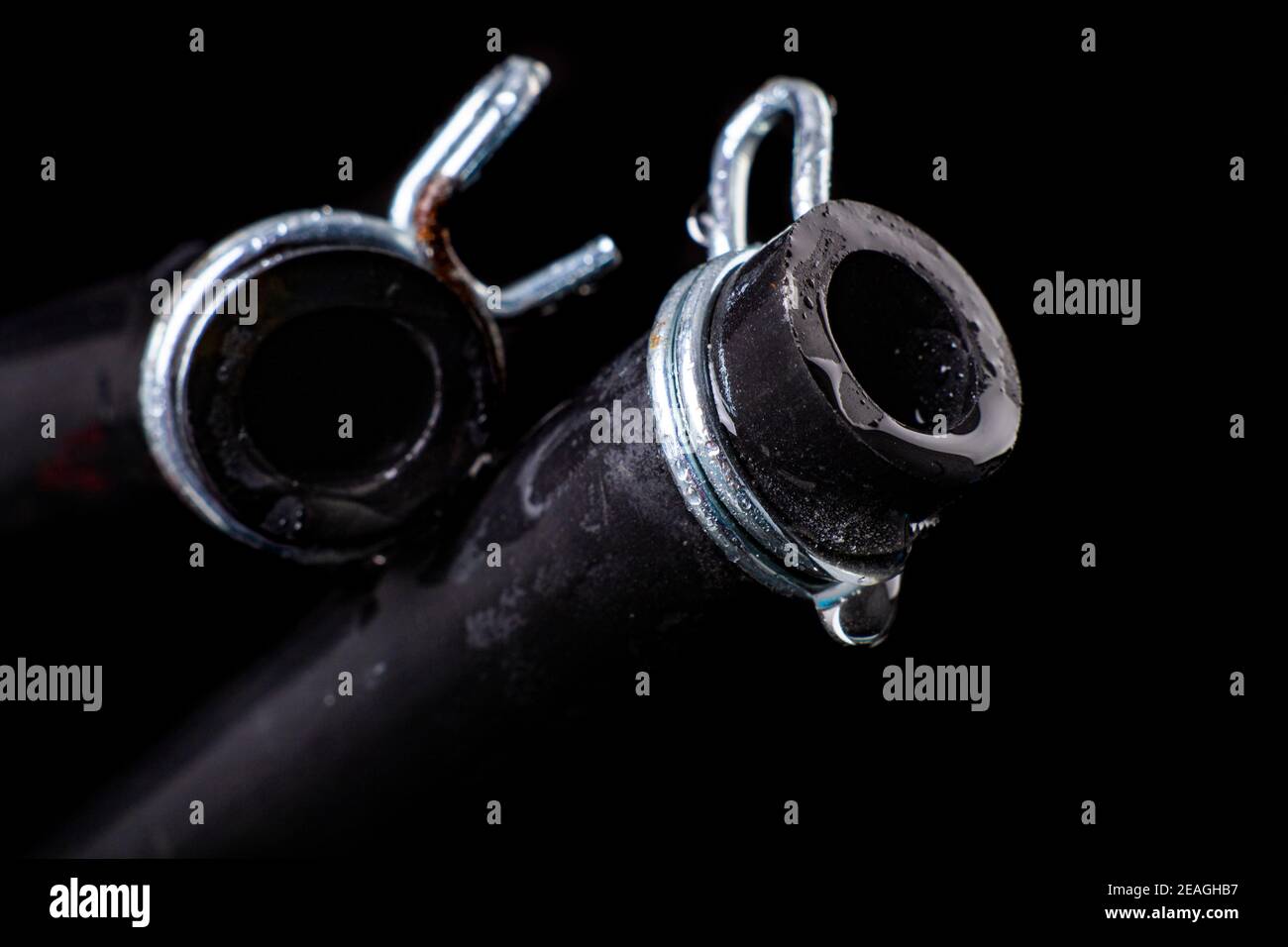Wet black hose with metal clamp. Accessories and spare parts for plumbers who renovate water and sewage systems. Black background. Stock Photo