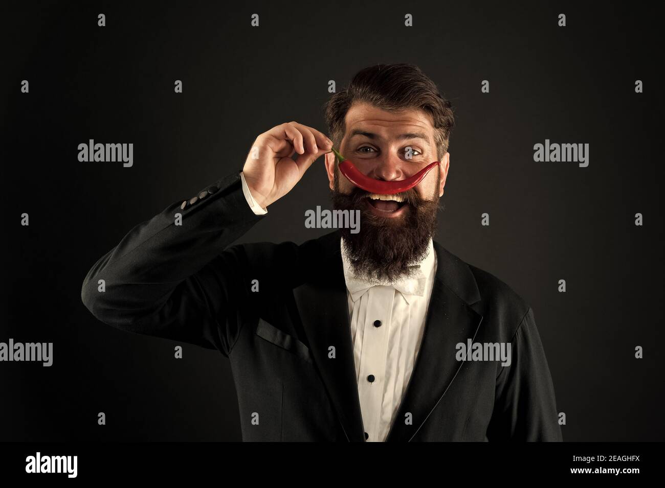 Pepper mustache. Bearded businessman hold chilli red pepper in hand. Guy hold Hot chilli pepper black background. Handsome macho likes spicy taste. Man hold pepper harvest. Barber funny face. Stock Photo