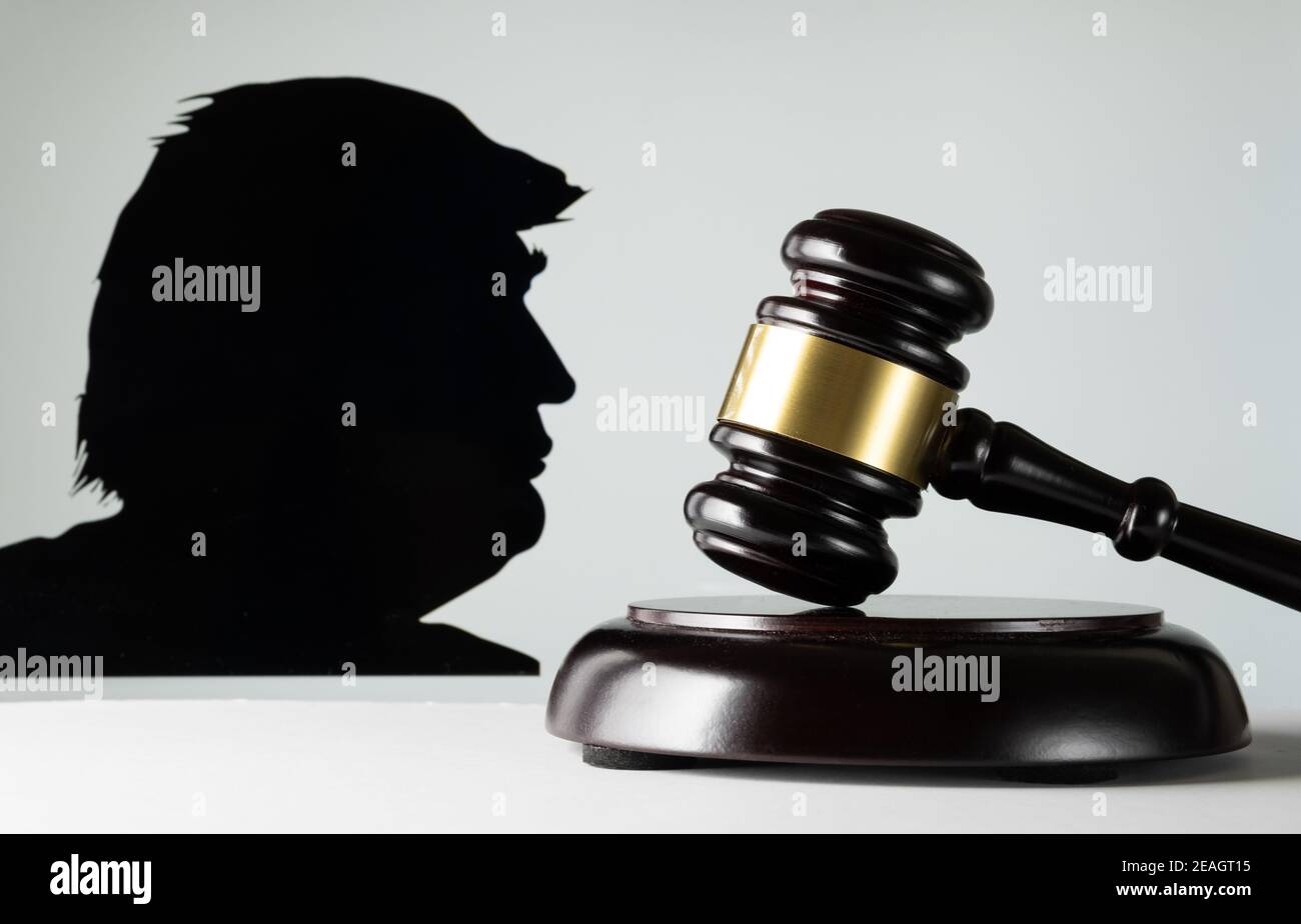 Donald Trump facing impeachment trial. Concept. Judge gavel on the front and Donald Trump blurred silhouette on the white screen background. Stock Photo