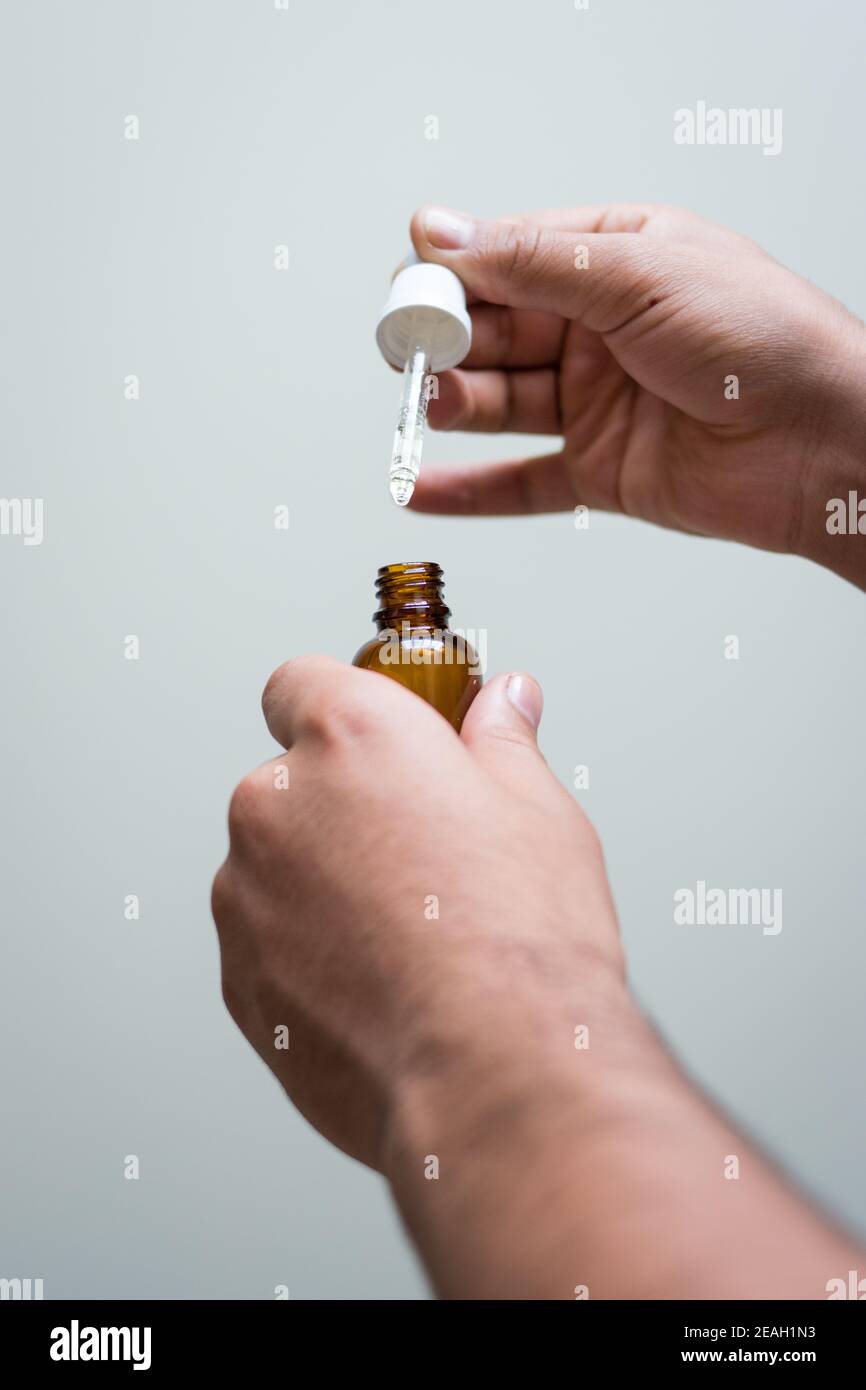 White hands using a dark glass dropper with a white background Stock Photo