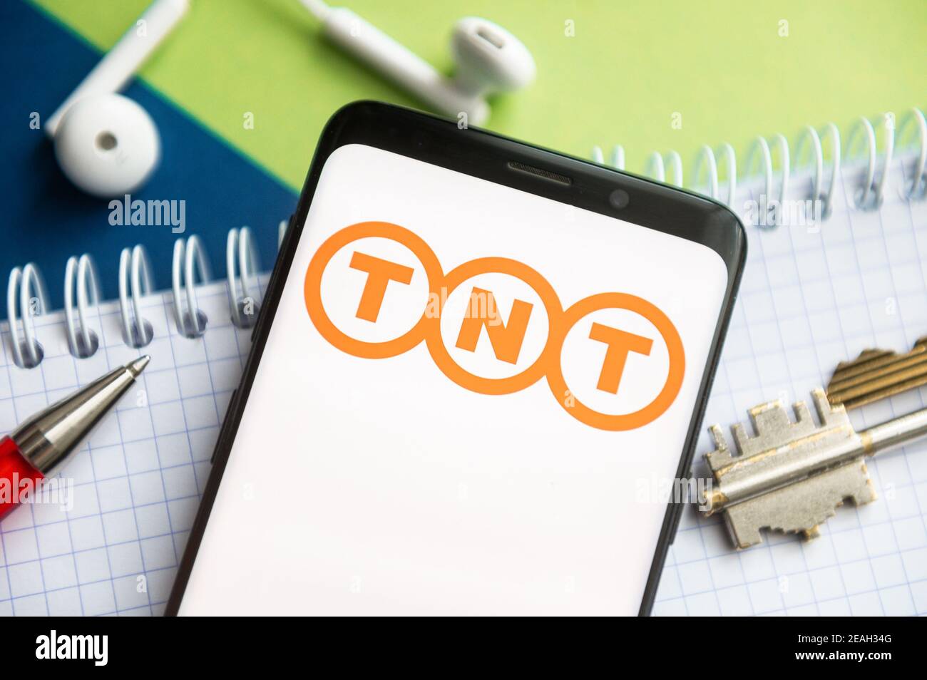 In this photo illustration a TNT logo seen displayed on a smartphone with a pen, key, book and headsets in the background. Stock Photo