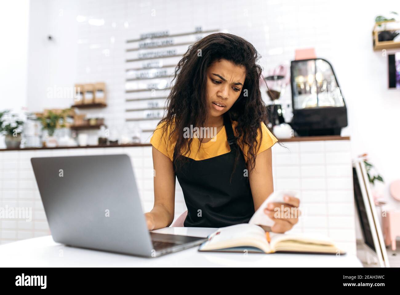 Unhappy young multiracial female barista or waitress, studying small business monthly financial statement, financial loss due to quarantine, bankruptcy Stock Photo