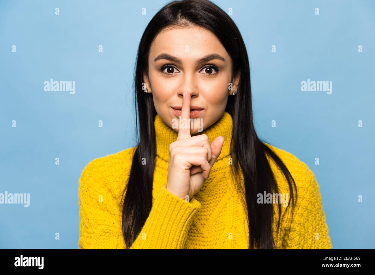 Portrait of cute caucasian young woman, shows gesture shhh, do not tell secret information, stands on isolated blue background Stock Photo