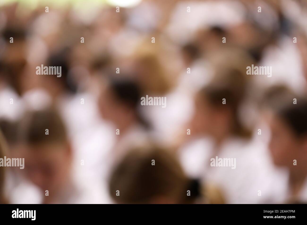 A deliberate artistic blurry shot of a large group of blurred people all wearing white shirts facing, sitting or walking in the same direction Stock Photo