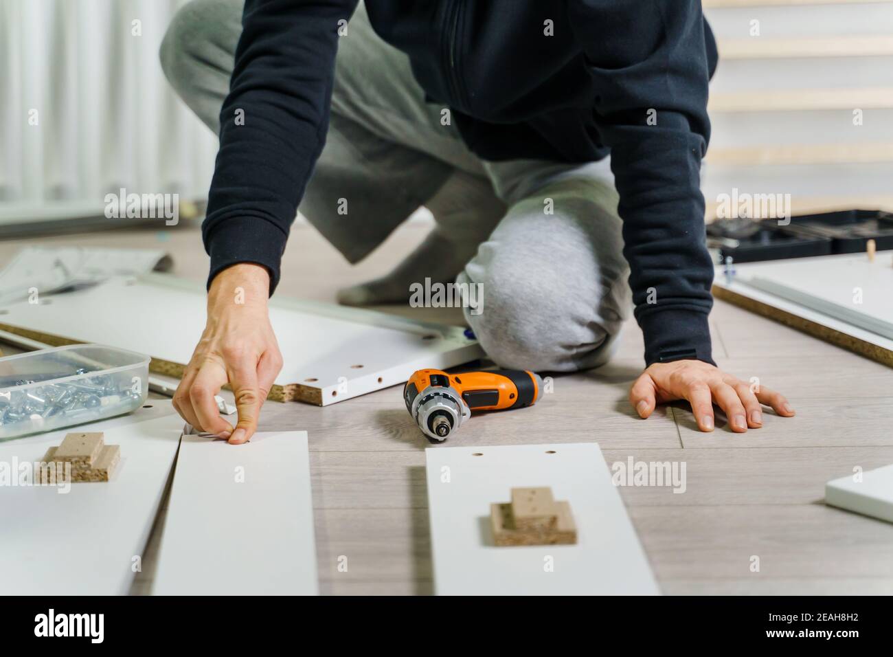 Close up on midsection of unknown caucasian man holding electric screwdriver while putting together Self assembly furniture of plywood screwing screws Stock Photo