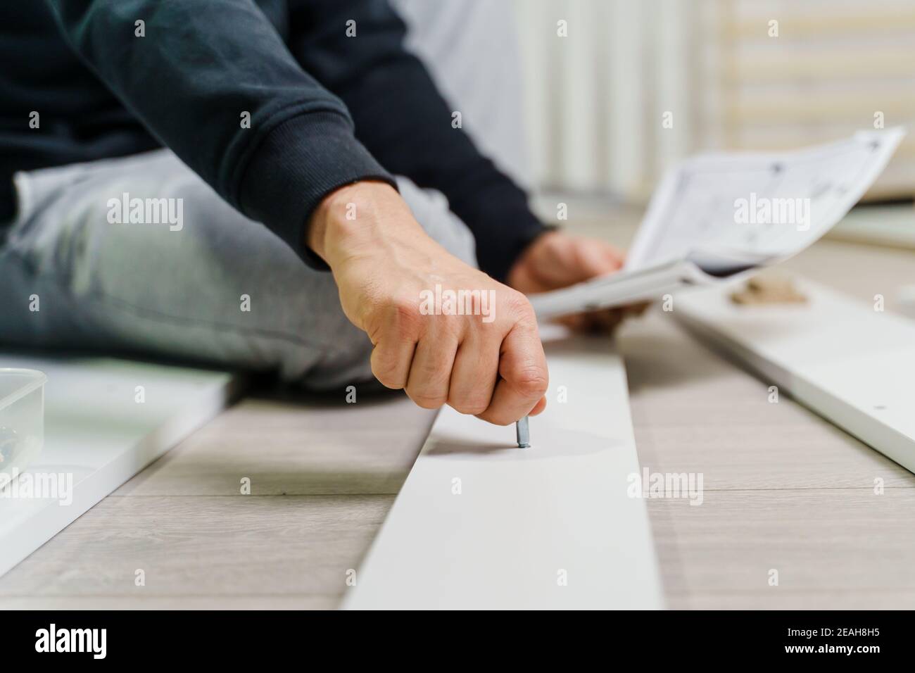 Close up on midsection of unknown caucasian man holding electric screwdriver while putting together Self assembly furniture of plywood screwing screws Stock Photo