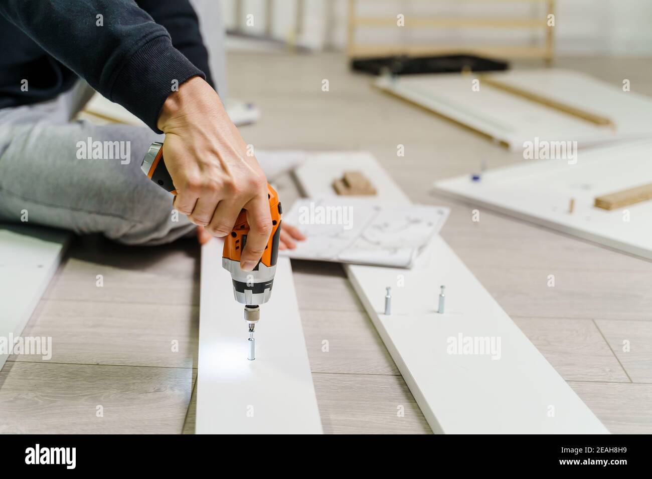 Close up on midsection of unknown caucasian man holding electric screwdriver while putting together Self assembly furniture of plywood screwing screws Stock Photo
