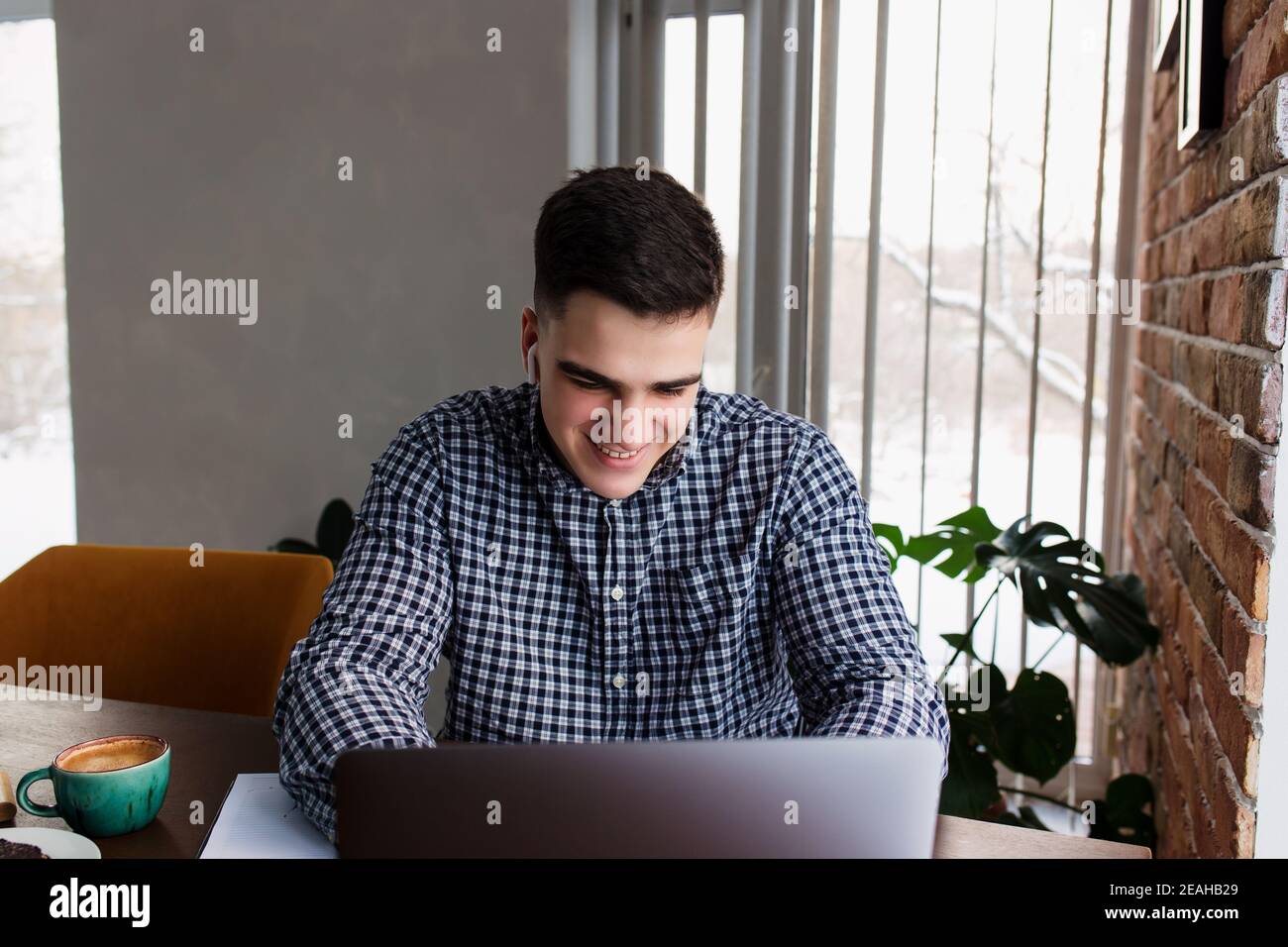 Smiling man working at laptop with a cup of coffee at home. Blurred background Stock Photo