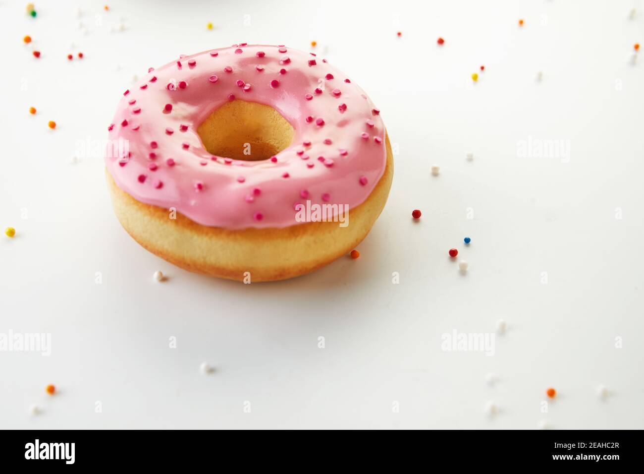 Pink donut with icing, sprinkles on white background. Stock Photo