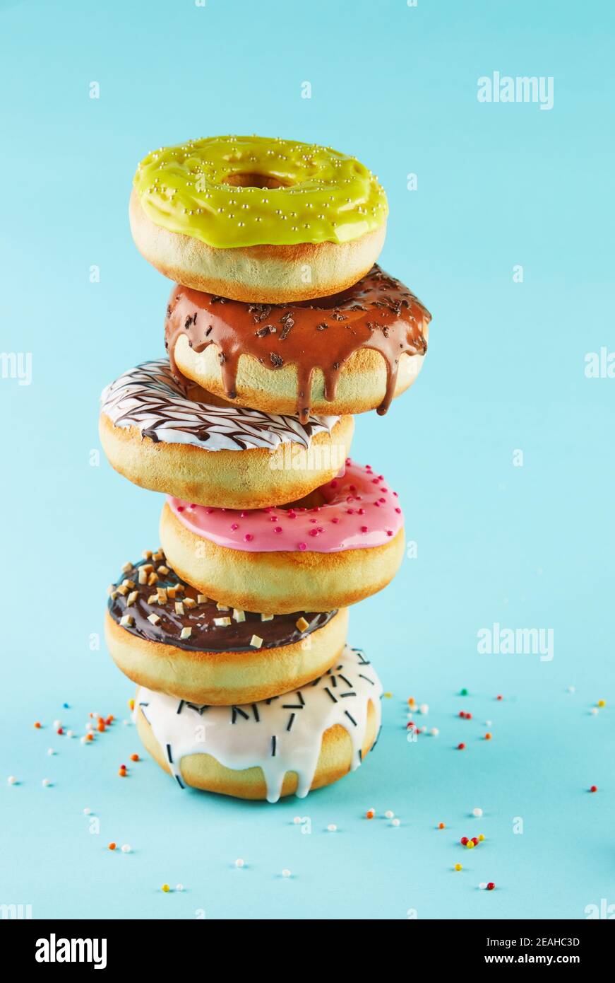 Multicolored donuts with icing and sprinkling stacked in a stack on a blue background. Stock Photo