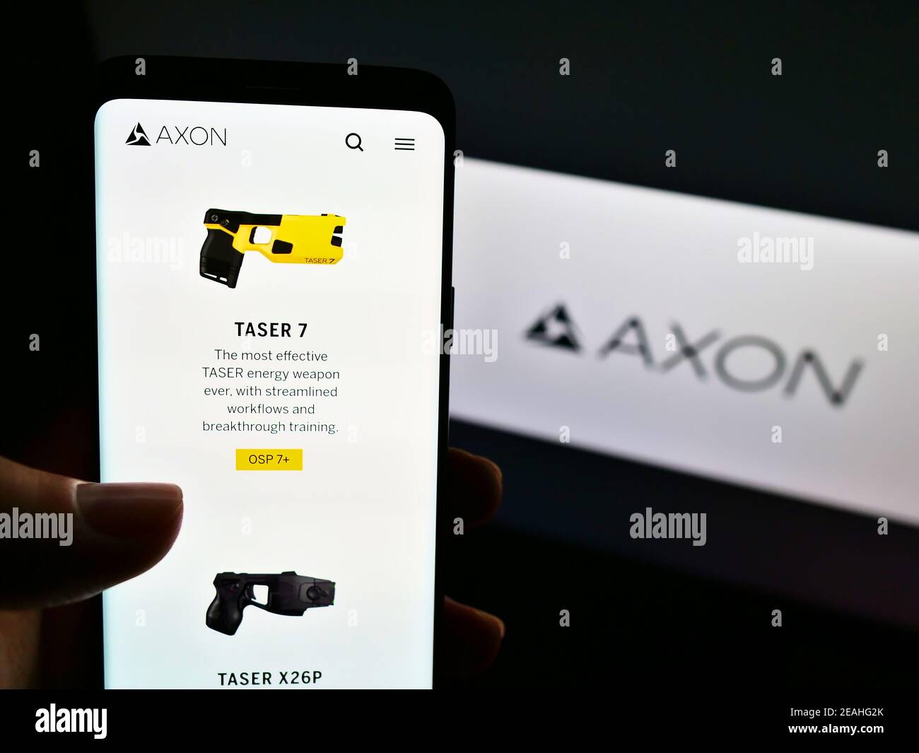 Person holding cellphone with product website of American weapon producer Axon Enterprise Inc. on screen with logo. Focus on center of phone display. Stock Photo