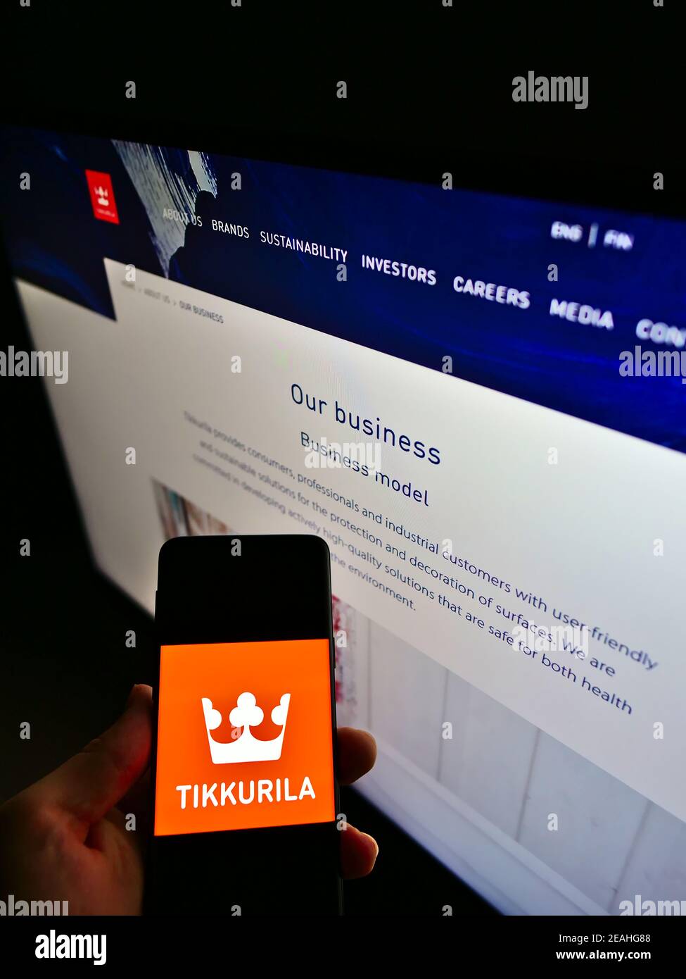Person holding mobile phone with logo of Finnish paint manufacturer Tikkurila Oyj on screen in front of company web page. Focus on phone display. Stock Photo