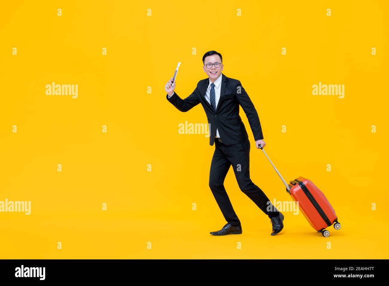 Full body of Asian man in formal business suit with baggae passport and boarding pass ready to go for traveling isolated on yellow background Stock Photo