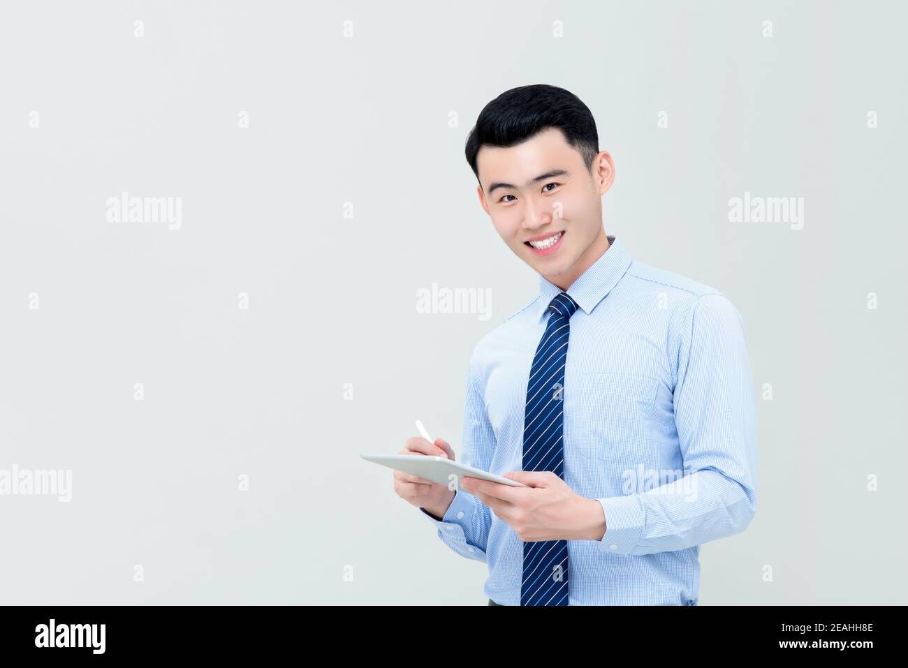 Young smiling Asian businessman using digital tablet with stylus pen isolated on gray background Stock Photo
