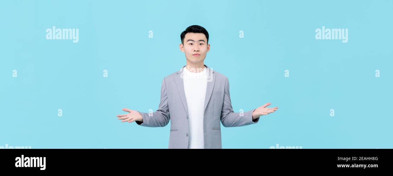 Young Asian man in semi-formal clothes doing open hand gesture isolated on light blue banner background Stock Photo